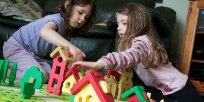 Dos niñas jugando con casas en el suelo y construyendo una pequeña ciudad.