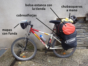 Bicicleta preparada para la lluvia con mapa enfundado en la cesta, cubrealforjas y tienda en la bolsa estanca