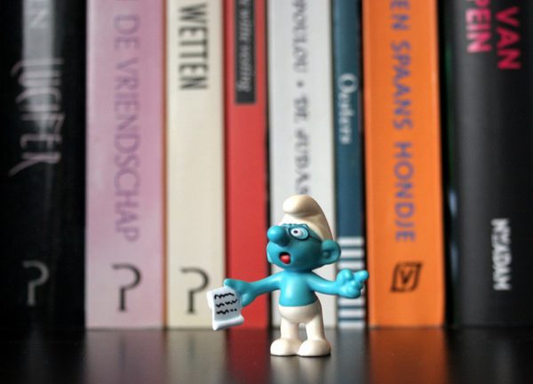 Muñeco de un pitufo con un papel frente a una pila de libros.